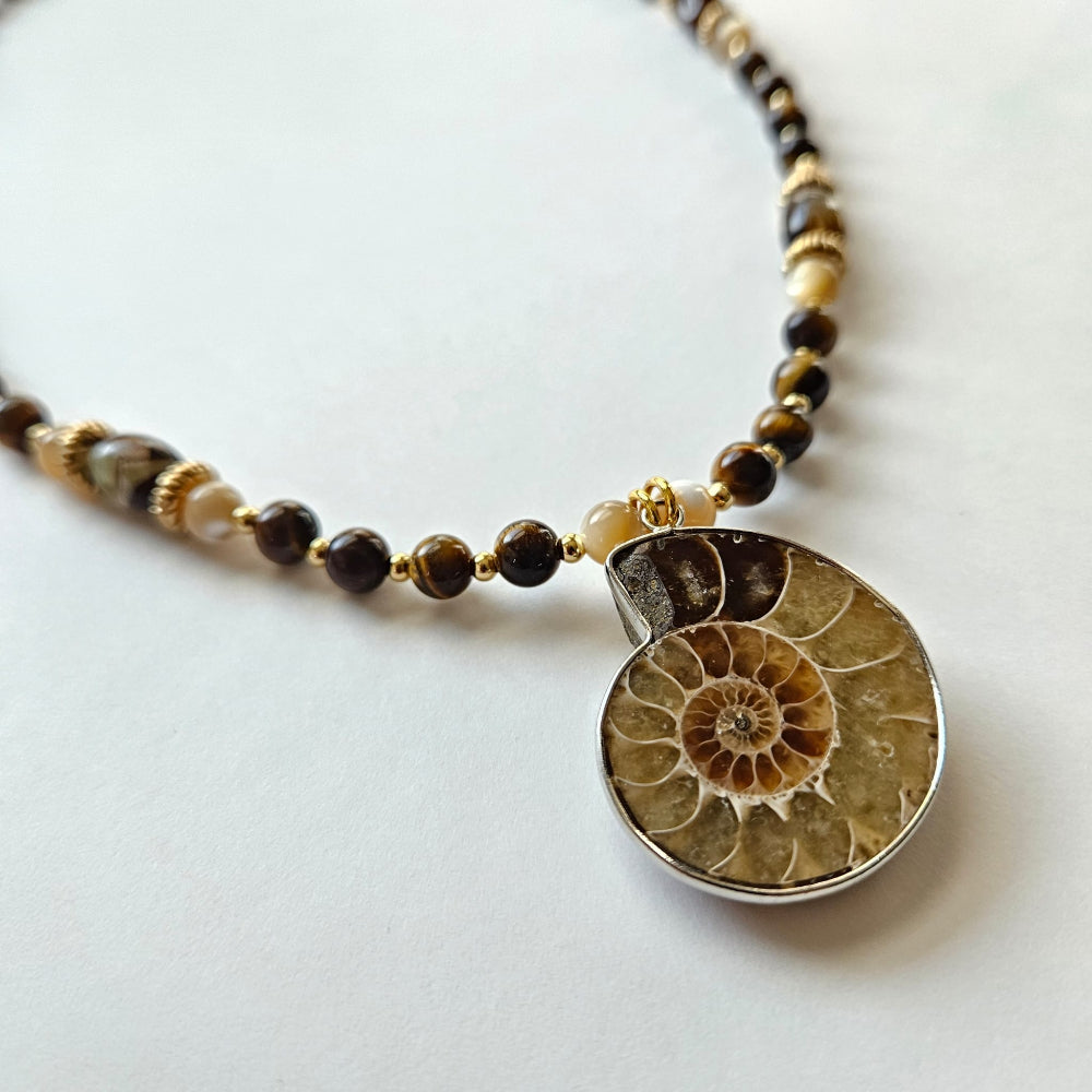 Fossilized ammonite pendant with tiger's eye beads, mother-of-pearl, gold-filled spacers, gold-color metal rondelles, chalcedony cylinders, and gold-plated clasp and findings.