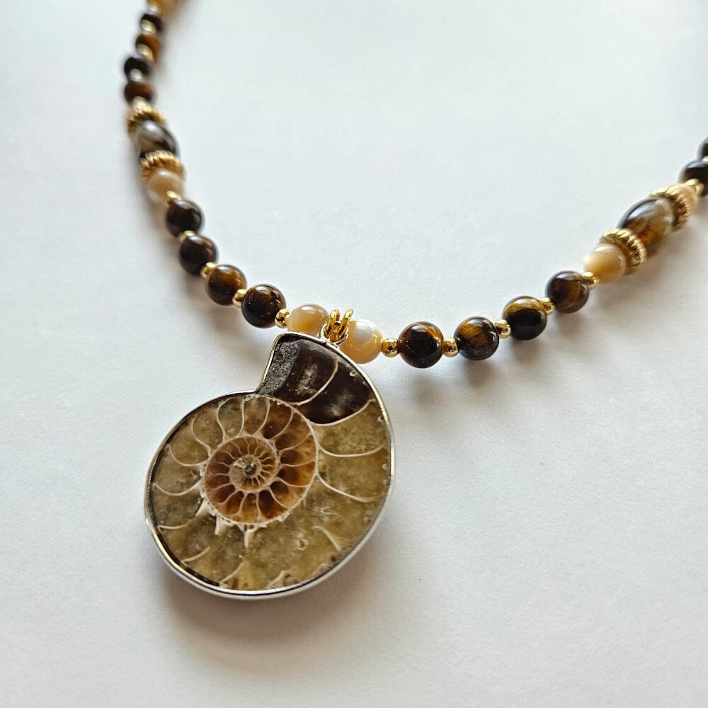 
                  
                    Fossilized ammonite pendant with tiger's eye beads, mother-of-pearl, gold-filled spacers, gold-color metal rondelles, chalcedony cylinders, and gold-plated clasp and findings.
                  
                