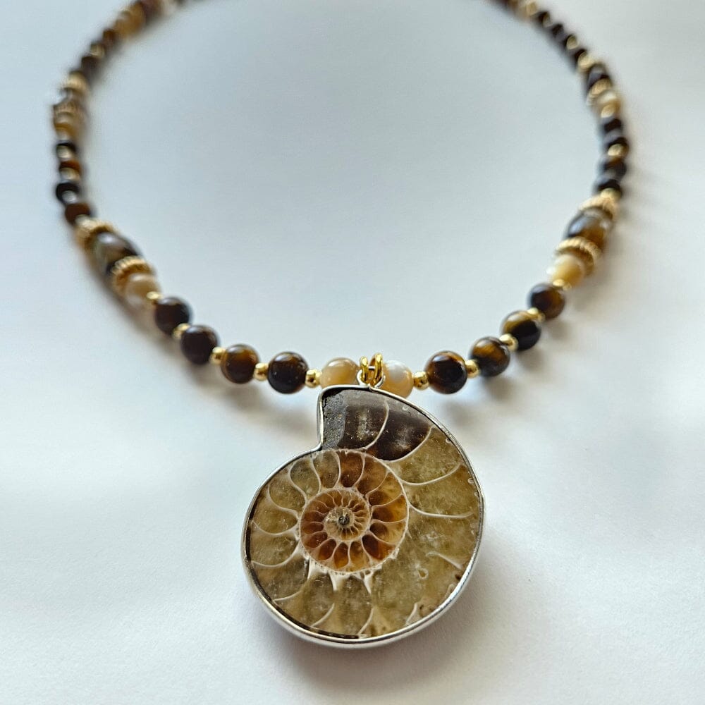 Fossilized ammonite pendant with tiger's eye beads, mother-of-pearl, gold-filled spacers, gold-color metal rondelles, chalcedony cylinders, and gold-plated clasp and findings.