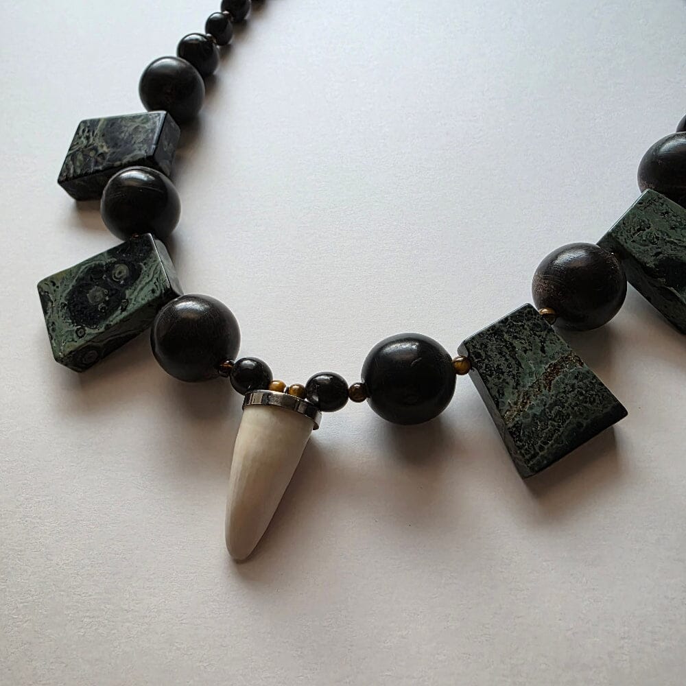 Necklace with black and green beads and a white tooth-like pendant on a light background