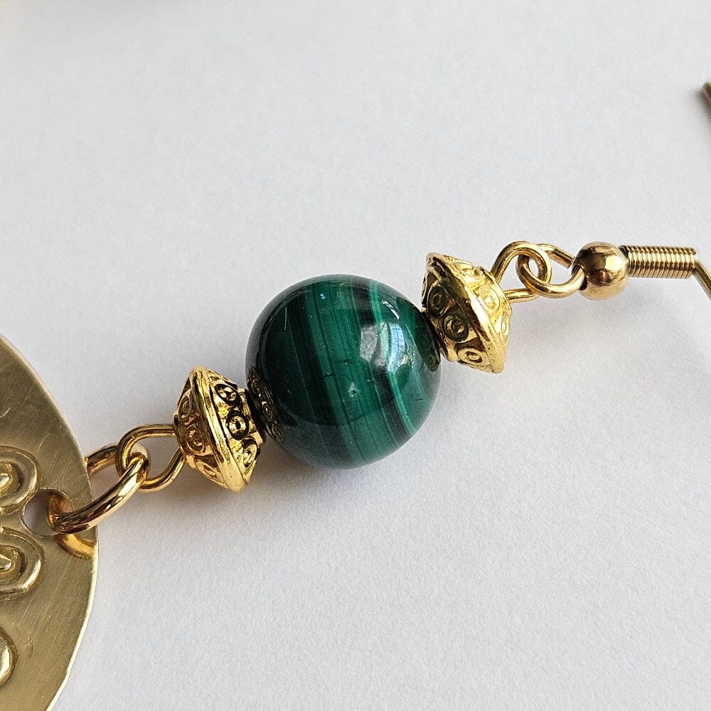 
                  
                    Brass agong medallions, malachite beads, gold tone conical motif design beads, gold-plated stainless steel ear wire and findings.
                  
                