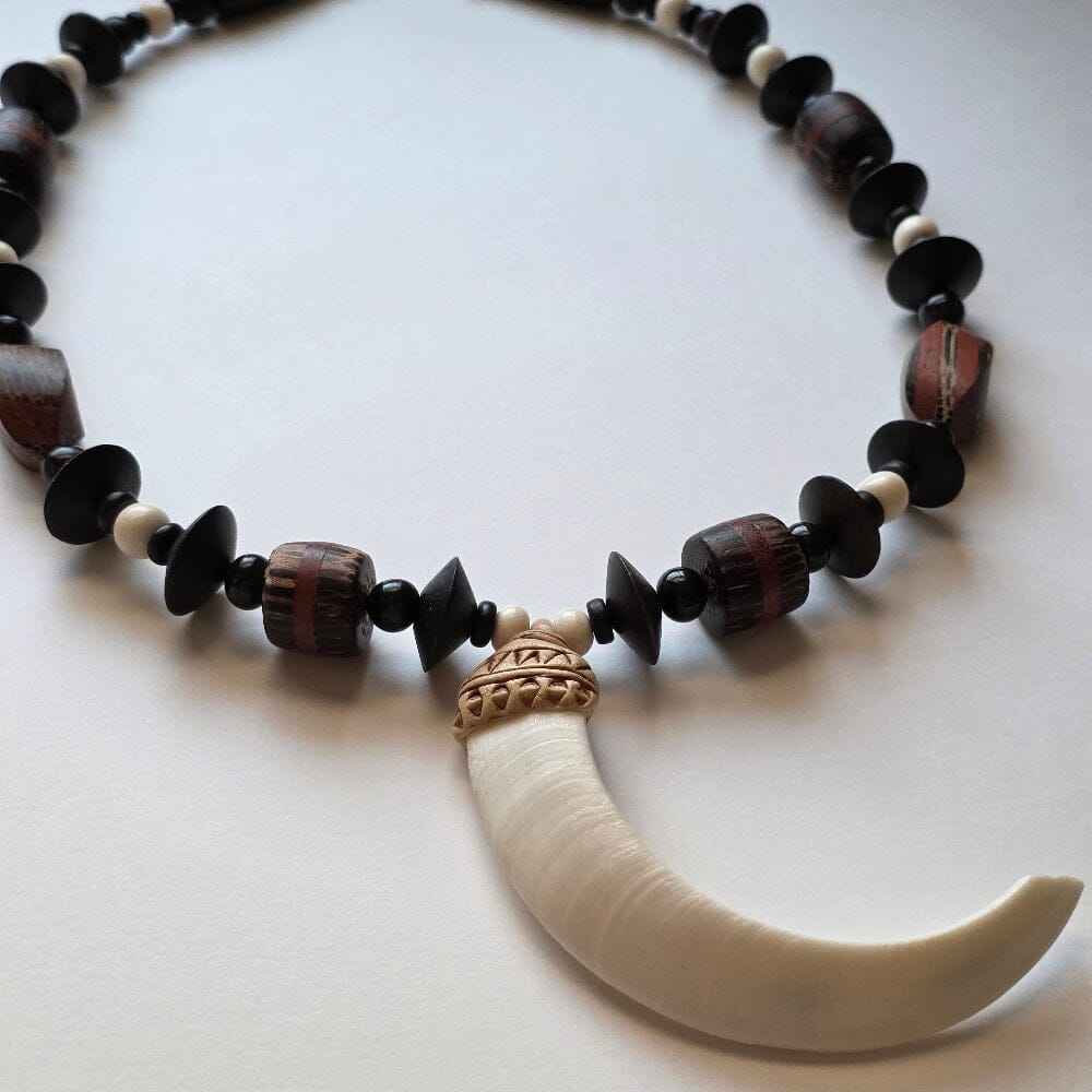 Necklace with black and brown beads and a white tusk pendant on a light background