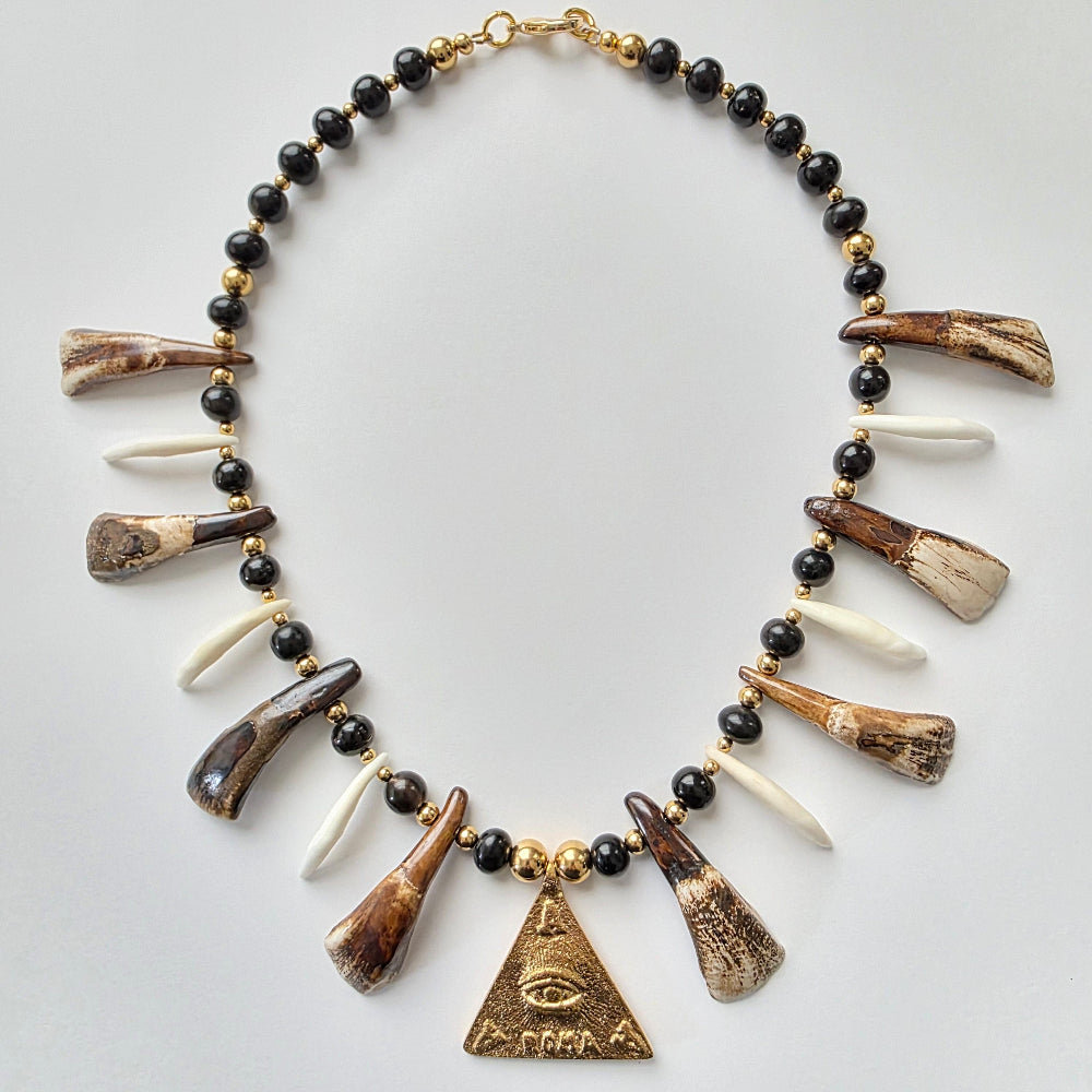 Necklace with black beads, tooth and horn elements, and a gold triangle pendant on a light gray background