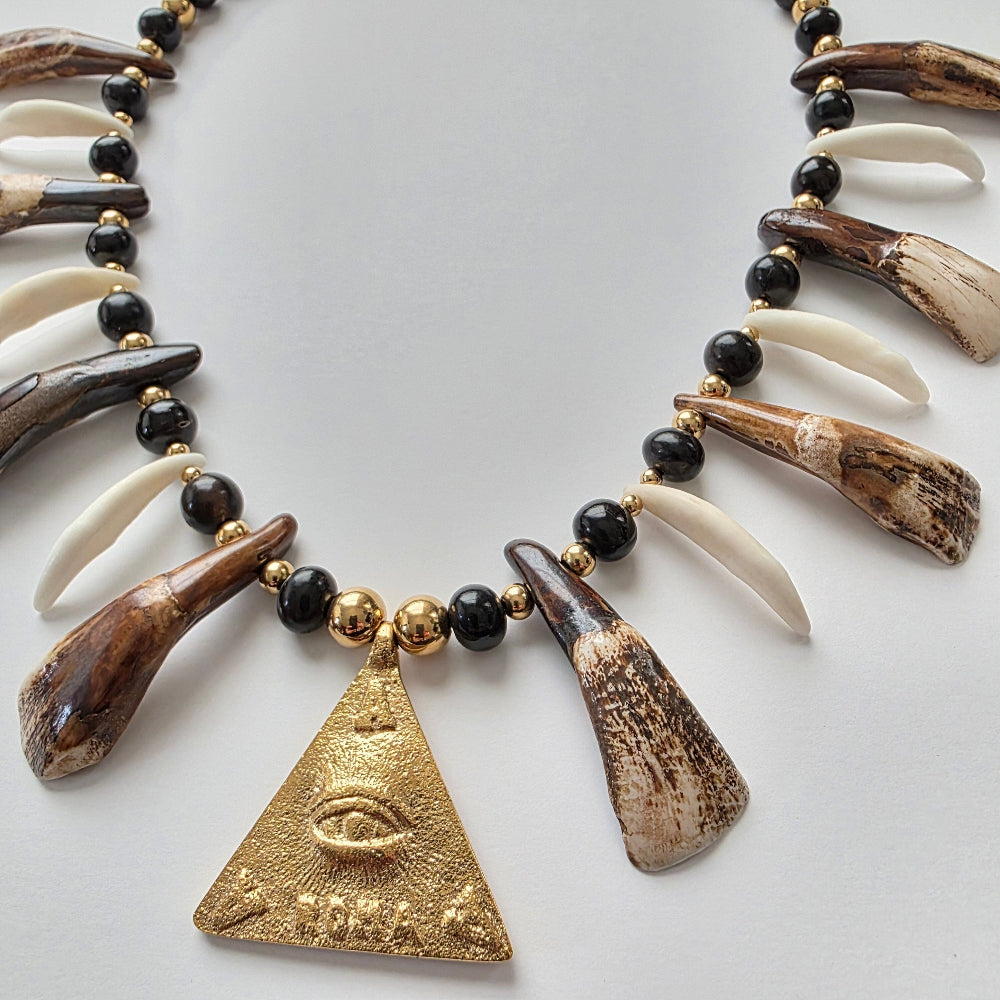 Necklace with water buffalo teeth, black beads, and a gold triangle pendant on a light gray background