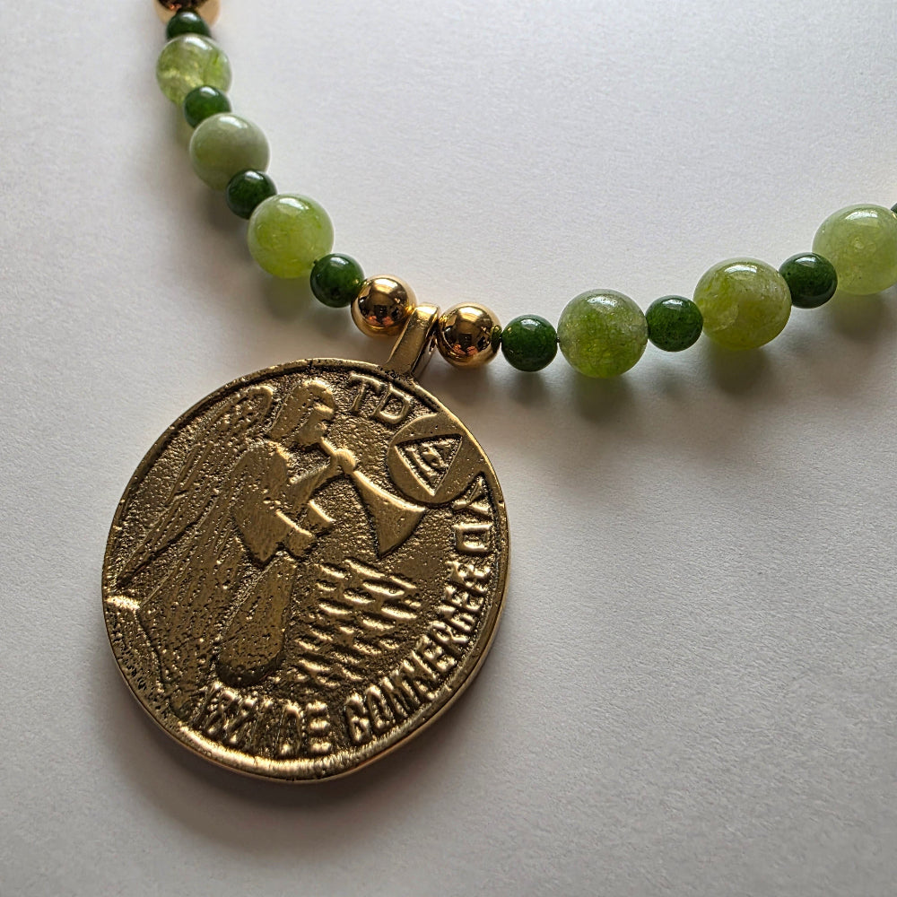 Necklace with green beads and a gold coin pendant on a light gray background