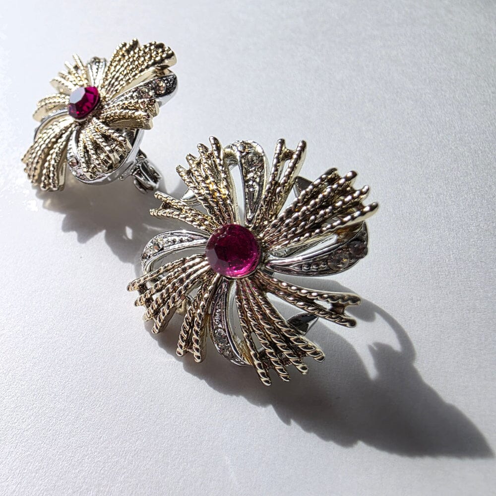 Pair of gold and silver earrings with red gemstones on a light gray background
