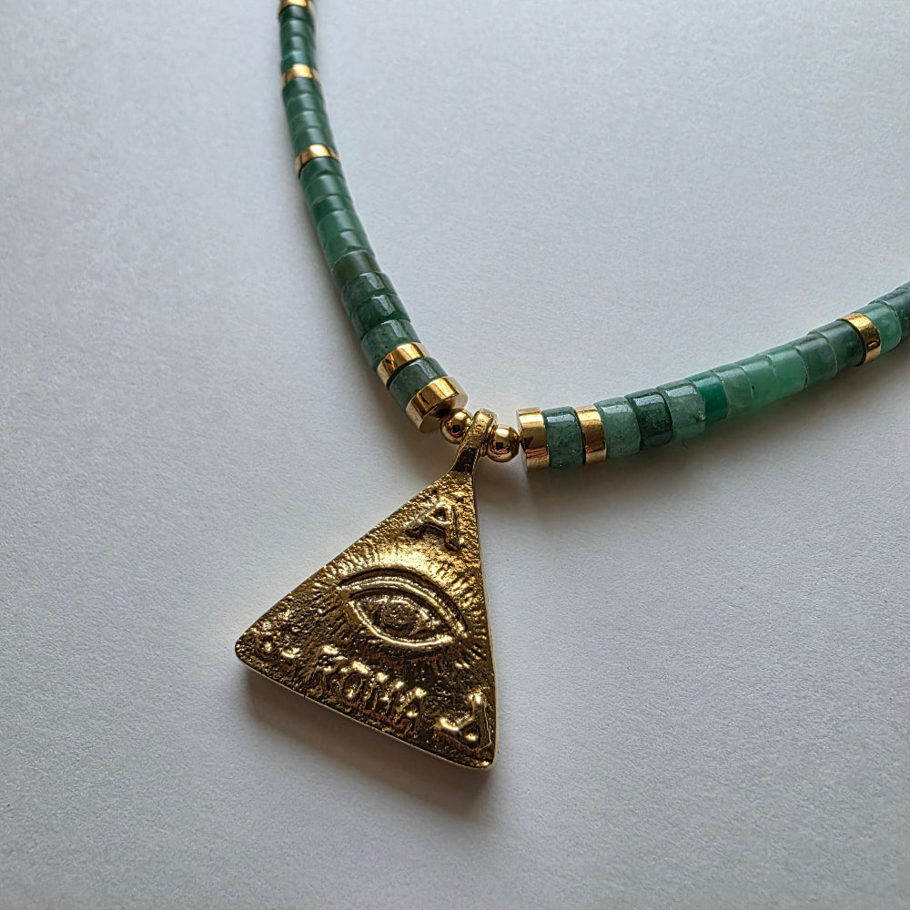 Necklace with green beads and gold triangle pendant on a light gray background