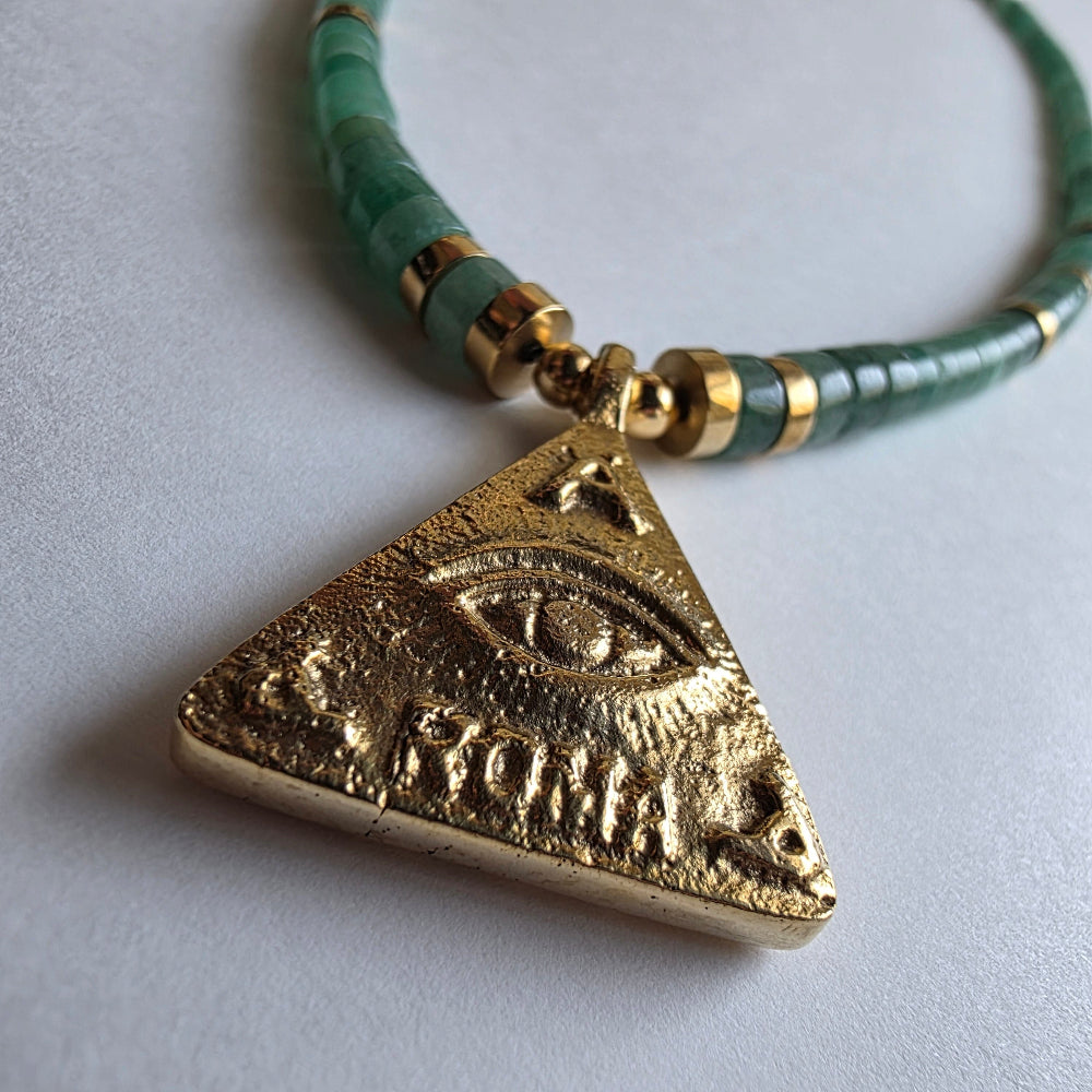 Gold triangle pendant with green beaded necklace on a light gray background