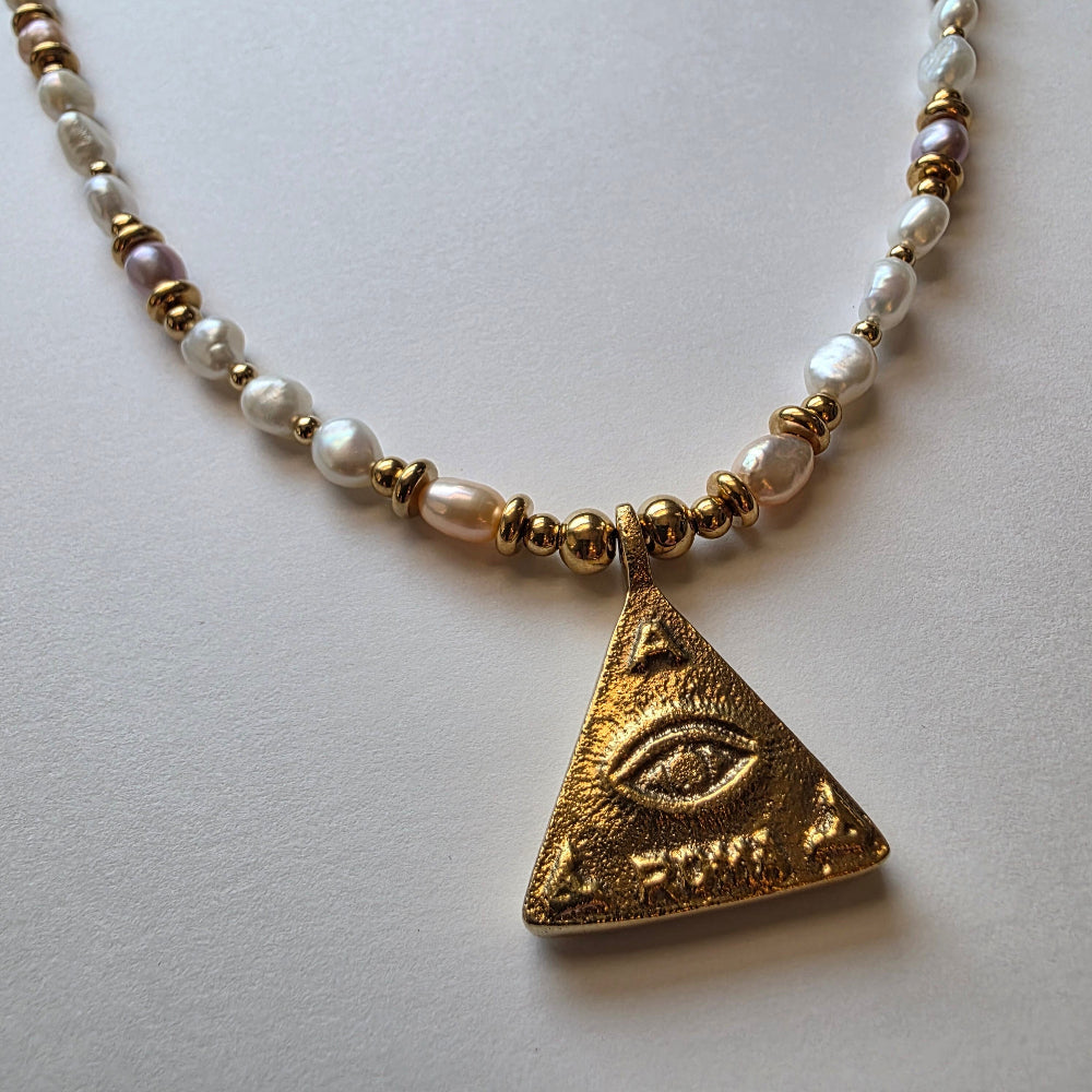 Necklace with gold and pearl beads and a triangular gold pendant on a light background