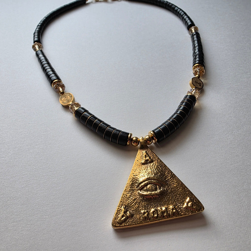 Necklace with black beads and gold triangle pendant on a light gray background
