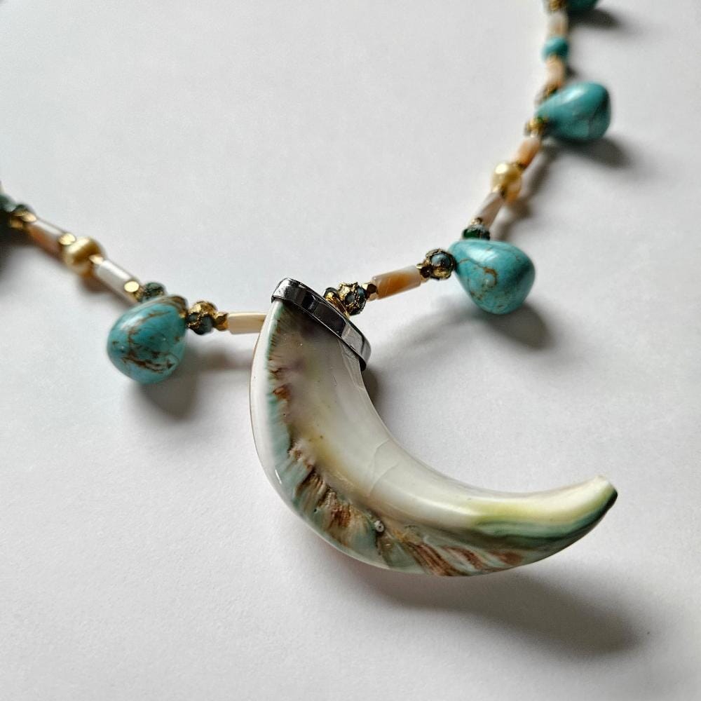 
                  
                    Rare giant green-banded turbo marmoratus shell tusk pendant from the Philippines. Necklace is beaded with dyed turquoise colored howlite teadrop beads with cloisonne, gold colored metal faceted spacers. mother-of-pearl tube beads and golden freshwater pearls from the Philippines.
                  
                