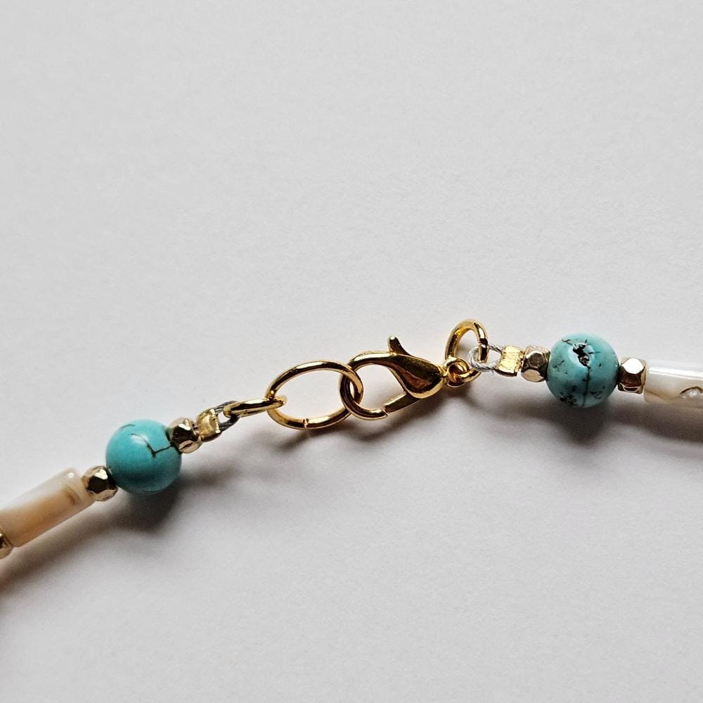 
                  
                    Detail of 18 k gold plated clasp and findings, dyed turquoise howlite beads, gold colored faceted metal spacers, and mother-of-pearl tube beads.
                  
                