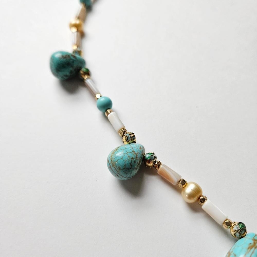 
                  
                    Detail of dyed turquoise colored howlite teadrop beads with cloisonne, gold colored metal faceted spacers. mother-of-pearl tube beads and golden freshwater pearls from the Philippines.
                  
                