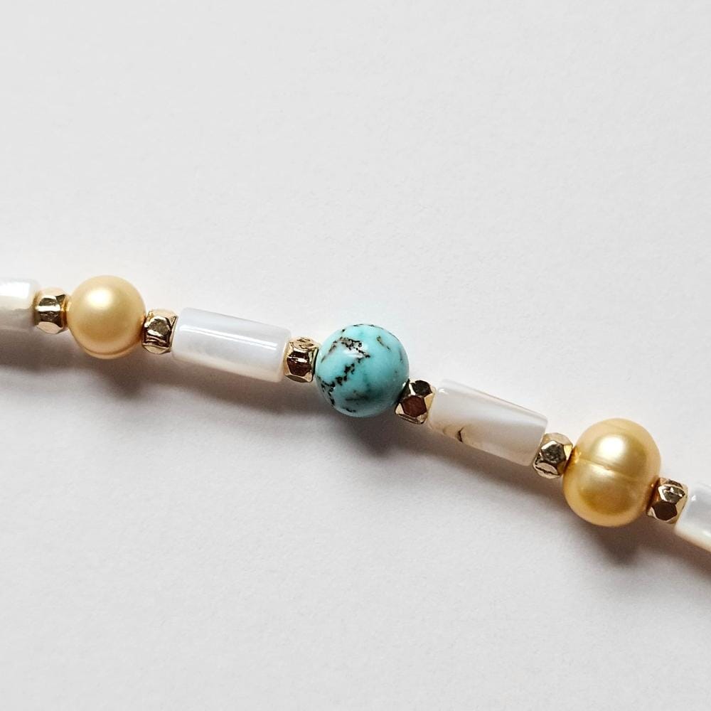 
                  
                    Dyed turquoise howlite bead, gold colored faceted metal spacers, and mother-of-pearl tube beads.
                  
                