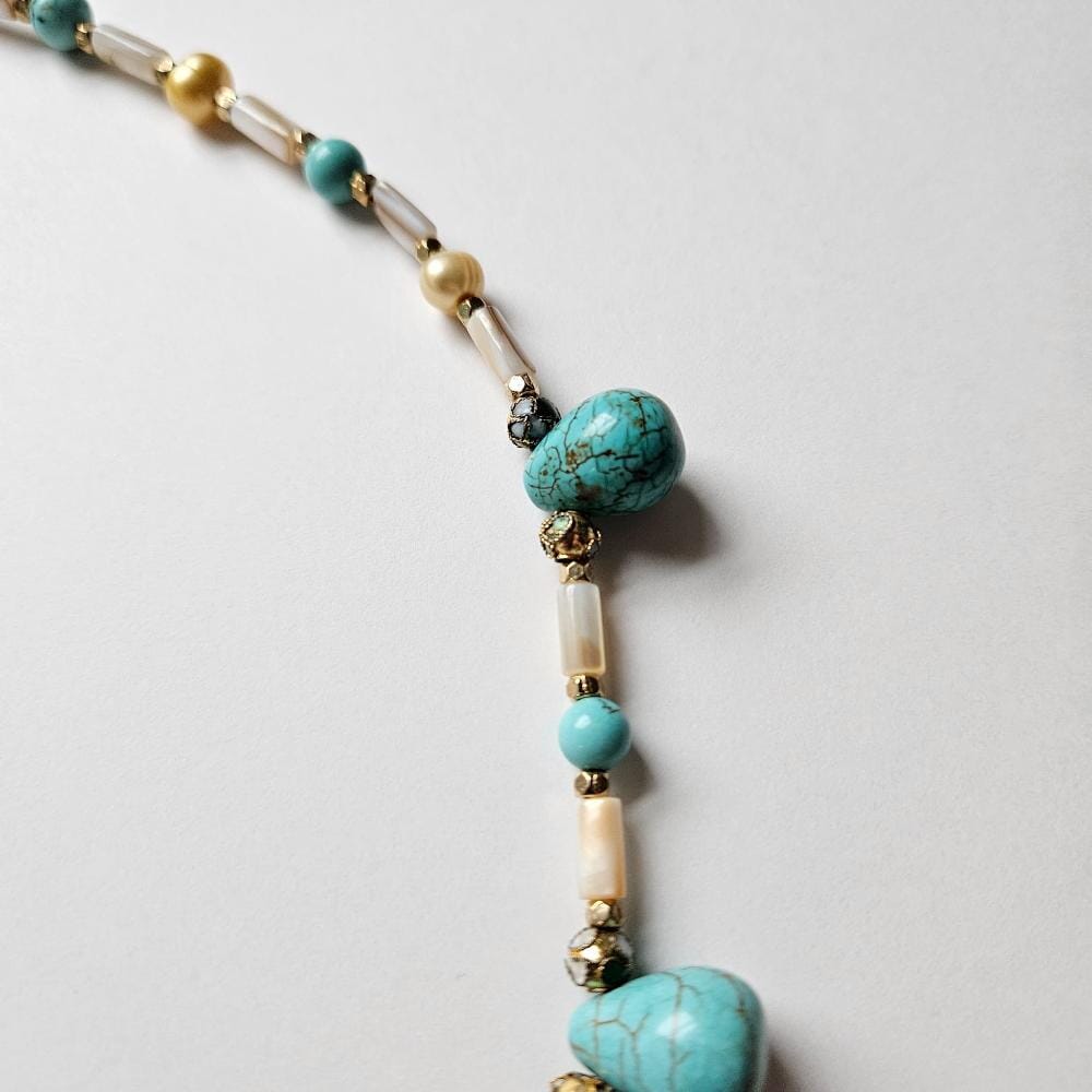 
                  
                    Up close detail of dyed turquoise colored howlite teadrop beads with cloisonne, gold colored metal faceted spacers. mother-of-pearl tube beads and golden freshwater pearls from the Philippines.
                  
                