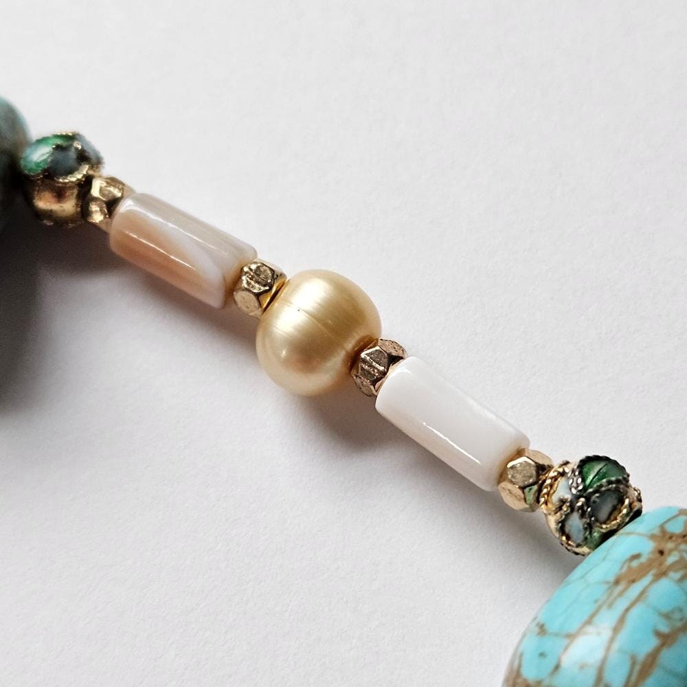 
                  
                    Mother-of-pearl tube beads and golden freshwater pearls from the Philippines with gold colored metal faceted spacers. Dyed turquoise colored howlite teadrop beads with cloisonne beads on both sides of the dyed turquoise colored howlite teardrop beads. 
                  
                